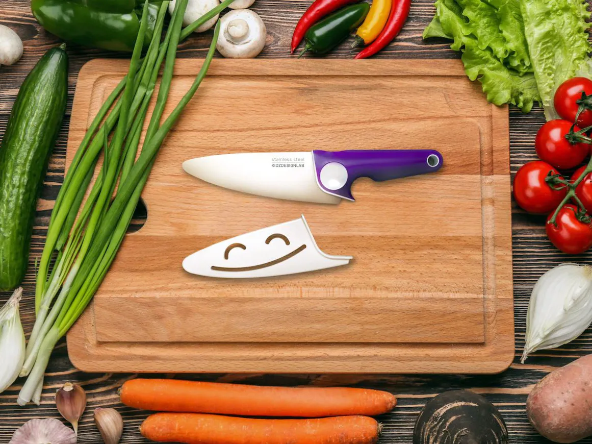 Chef's knife on a cutting board surrounded by fresh vegetables